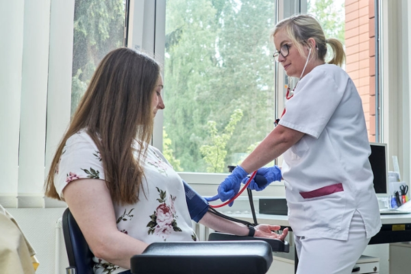 Blutdruckmessung bei einer sitzenden Rehabilitandin durch eine Mitarbeitende Blutdruckmessung bei einer sitzenden Rehabilitandin durch eine Mitarbeitende