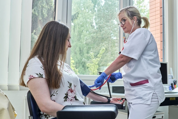 Blutdruckmessung bei einer sitzenden Rehabilitandin durch eine Mitarbeitende